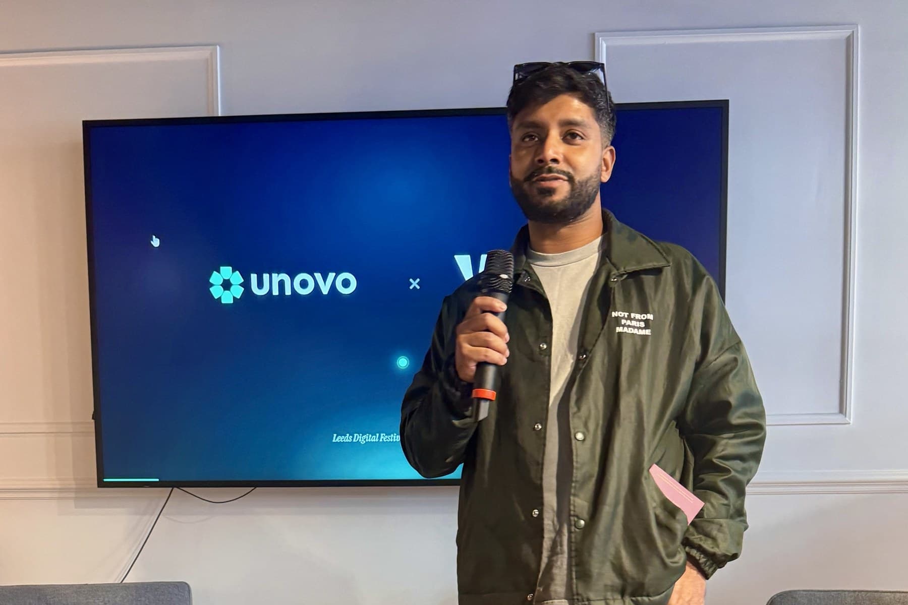 Tanvir Hassan holding a microphone in front of a screen showing the Unovo and Venture Community logos.