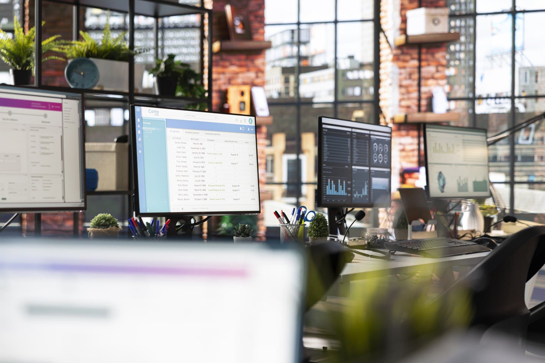 A row of desktop monitors showing dashboards and spreadsheets in an empty office with brick walls and large windows.